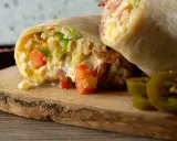 Pyszna tortilla z jajecznicą, pomidorami i papryką, podana na drewnianej desce z plasterkami jalapeno.