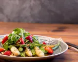 Ein frischer Spargelsalat mit Erdbeeren, Rucola und Pinienkernen, appetitlich auf einem Teller angerichtet.