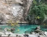 La source de la Sorgue, une eau turquoise limpide émergeant d'une falaise rocheuse, entourée de végétation et d'arbres aux feuilles d'automne.