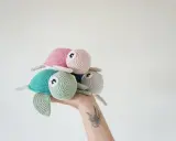 Una mano sostiene un trío de adorables tortugas a crochet: una verde menta, una rosa y una gris claro.