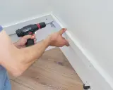 Pose d'une placo sur ossature bois. Un artisan utilise une visseuse pour fixer une plaque de plâtre sur une structure en bois.