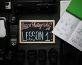 Szkolenie online dla fotografów: "Learn Photography LESSON 1". Na zdjęciu sprzęt fotograficzny, notatki o ISO, ekspozycji, przysłonie i czasie naświetlania.