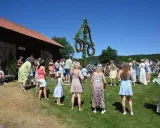 Folk dansar runt midsommarstången på midsommar afton. En vacker sommardag med klarblå himmel.