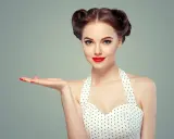 Kobieta w stylu pin up, z burzą loków i czerwoną szminką, prezentuje dłoń. To lata 50. w pełnej krasie.