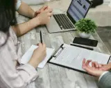 Réunion pour une contre-expertise assurance : un contrat est sur la table, un ordinateur portable ouvert, et des mains discutent des détails.