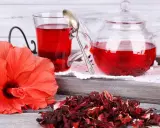 Orzeźwiająca herbatka z hibiskusa, podana w szklanym dzbanku i kubku, obok świeżego kwiatu i suszonych płatków.