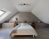 Chambre sous comble avec lit douillet, velux et décoration murale en bois.