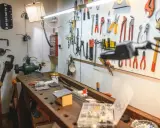 Warsztat domowy pełen narzędzi i pomysłów na majsterkowanie. Widać tu imadło, szlifierkę, mnóstwo kluczy, śrubokrętów i innych przyrządów.