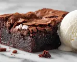 Un carré de tarte brownie, dense et chocolaté, avec une boule de glace à la vanille fondante. Un délice gourmand.