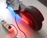 Un chargeur pour trottinette électrique est branché sur une multiprise. La trottinette est éclairée par des LED bleues et rouges.