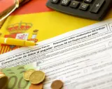 Documentos fiscales españoles, calculadora, bolígrafo amarillo y dinero, listos para cuando se pagan impuestos en España.
