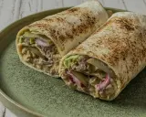 Zwei saftige Big Mac Wraps mit Hackfleisch, Salat, Gurken und Zwiebeln auf einem grünen Teller.
