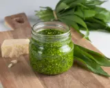 Pesto ail des ours fait maison dans un bocal, avec du fromage et des feuilles fraîches sur une planche en bois.