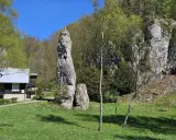 Imponująca skała Igła Deotymy góruje nad zieloną polaną, obok której stoi drewniany domek.