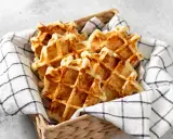 Un panier rempli de gaufres dorées, parfaites pour une recette gaufre rapide. Elles sont présentées sur une serviette à carreaux noirs et blancs.