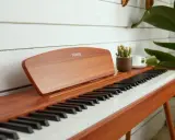 Eleganckie pianino cyfrowe Donner, idealne do nauki gry na pianinie online. Obok stoi filiżanka kawy i mała roślinka.