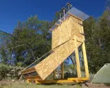 Un sechoir solaire artisanal en bois, avec un panneau incliné vitré, sous un ciel bleu.