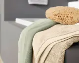 Weiche bad textilien in sanften Farben, darunter ein hellgrünes und ein beigefarbenes Handtuch, liegen neben einem natürlichen Schwamm auf der Kante einer Badewanne.