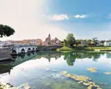 Ponte di Tiberio e il fiume Marecchia a Rimini a settembre, con riflessi sull'acqua e un cielo azzurro con nuvole bianche.