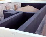 Fundament budowy z ciemnych bloczków, z nasypem piasku wewnątrz.