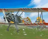 Ein Stearman Flugzeug mit zwei Männern an Bord fliegt über ein grünes Feld. Einer repariert etwas, der andere hält sich fest.