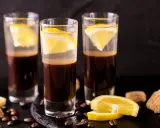 Drei Gläser mit Espresso und Zitrone, ein italienischer Genuss. Kaffeebohnen und Zuckerwürfel liegen daneben.