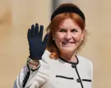 Sarah, hertiginna av York, vinkar glatt med en svart handske på sig. Hon bär en elegant ljus jacka med svarta detaljer och smycken.