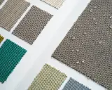 Próbki tkanin, jedna z nich z kroplami wody, pokazuje, co to znaczy water repellent – materiał nie wchłania płynów.