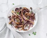 Radicchio in padella, caramellato e profumato, servito su un piatto bianco con un tocco di erbe aromatiche.