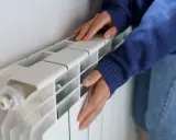 Manos frías tocan un radiador blanco que no calienta.
