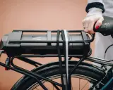 Main d'une femme tenant la selle d'un vélo électrique, avec la batterie visible sur le porte-bagages. Idéal pour tester la batterie du vélo.