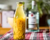 Bouteille de rhum arrangé mangue, avec des morceaux de fruits jaunes et des épices.