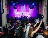 Festligt event med "Old School Brunch" i Stockholm. Människor sitter vid borden, en artist uppträder på scenen under lila ljus.
