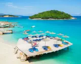 Rajskie widoki na **Albania najpiękniejsze plaże**. Turkusowa woda, piaszczysta plaża i drewniany pomost z leżakami.