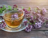Aromatyczna herbata z oregano w szklanej filiżance, otoczona gałązkami z kwiatami. Napar ten znany jest ze swoich właściwości wspomagających trawienie i działających antybakteryjnie.
