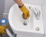 Manos enguantadas instalan el desagüe para cambiar el sifón del lavabo.