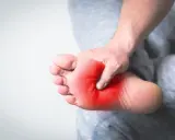 Ból w podeszwie stopy, zaznaczony czerwienią, uciska dłoń.
