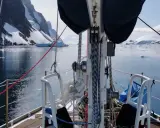 Voile sur un voilier dans un fjord glacé, avec des montagnes enneigées et des icebergs. Le **pen duick 600** navigue paisiblement.