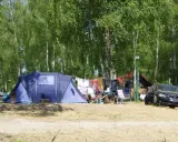 Idealne miejsce, gdzie pod namiot nad jezioro. W tle las, a przed namiotem rozłożone krzesła i suszące się pranie.