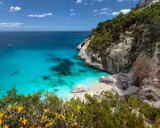 Traumhafter Strand Sardinien mit türkisfarbenem Wasser, Felsen und grüner Vegetation. Eine kleine Bucht lädt zum Entspannen ein.