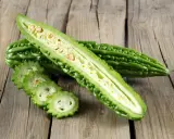 A halved bitter melon plant reveals its seedy interior, with sliced rounds fanned out on a rustic wooden surface.