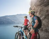 Ein Paar genießt die Aussicht auf den Gardasee während einer E-Bike-Tour. Die Berge und das klare Wasser bilden eine atemberaubende Kulisse.