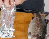 Vorbereitung für das Grillen: Ein Fisch wird in Alufolie gewickelt, bereit für den Weber Grill.