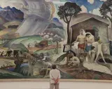 A mural depicting rural life and labor, reminiscent of the Wyeth family artists' style, with figures tending to livestock and fields under a dramatic sky.
