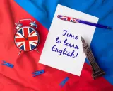 Budzik z flagą UK, długopis i napis "Time to learn English!" na tle brytyjskich barw. Czas na naukę!
