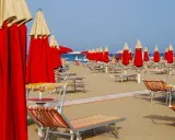 Filetto di ombrelloni rossi e lettini pronti per accogliere i bagnanti sulla costa di Rimini.