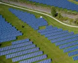 Große Solaranlage auf einer grünen Wiese mit Gleisen im Hintergrund.