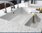 Évier de cuisine moderne en quartz ou granit, avec robinetterie chromée et une serviette pliée.