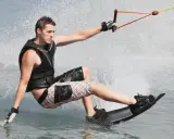 Młody mężczyzna na desce, ciągnięty przez linę, pokazuje, **wakeboarding co to** jest – sport wodny pełen adrenaliny i zabawy.