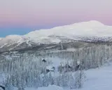 Snötäckta berg och skog med små stugor, en idyllisk vy över mindre skidorter Sverige i skymningen.